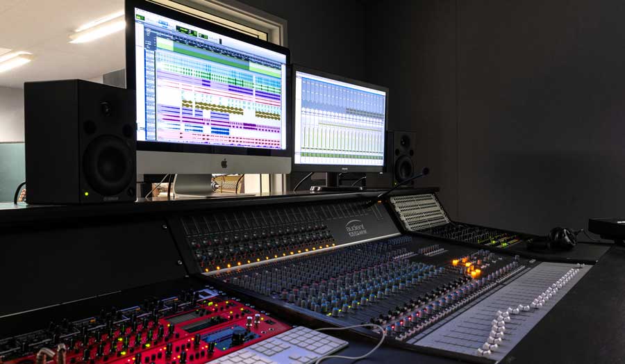 a mixing deck and 2 screens in a music control room