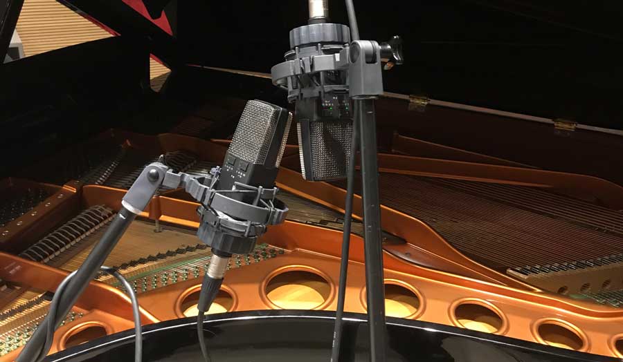 a close up of an open and lit up Bosendorfer grand piano with 2 microphones near it for recording