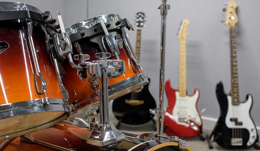 a drum kit in the forefront and 3 guitars in the background leaning against a wall