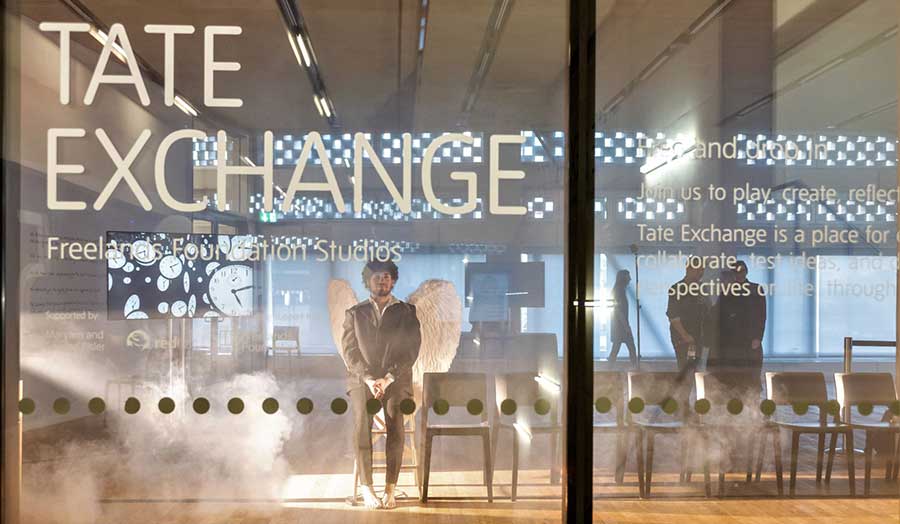 A performance artist dressed as an angel seen through the window of the Tate Exchange exhibition
