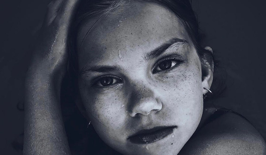 Black and white image of young girl with wet face staring towards camera 