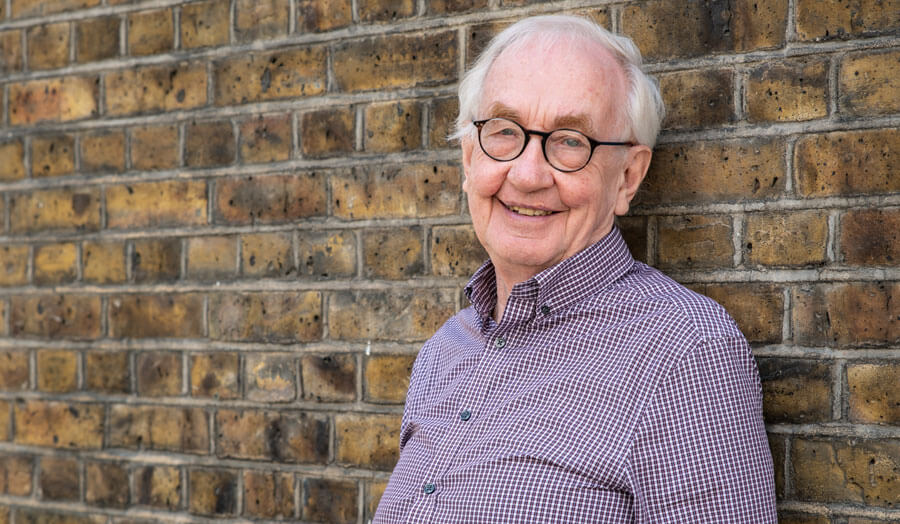 Professor Fergus Nicol leaning against a brick wall and smiling to camera.
