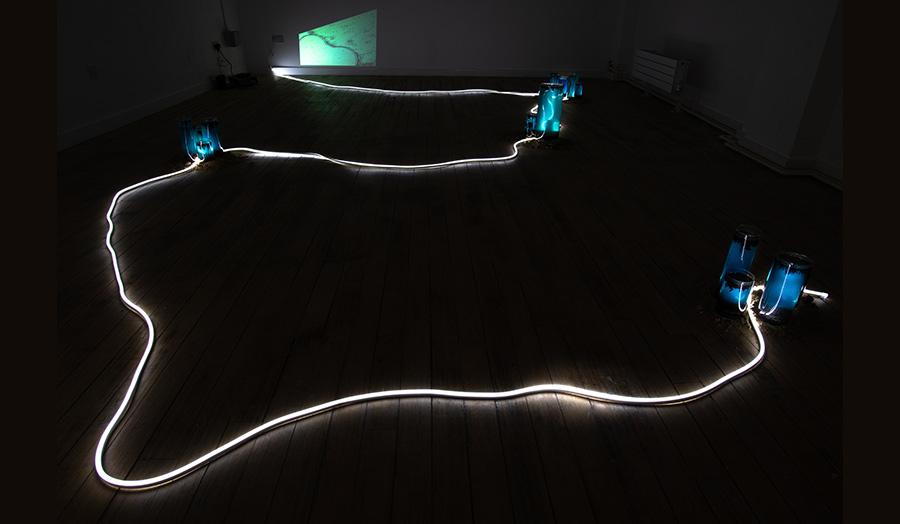 A neon light tube swirling on a dark room's wooden floor 
