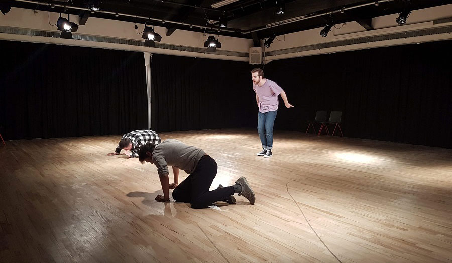 Two men kneeling down on a wooden floor while another man is standing
