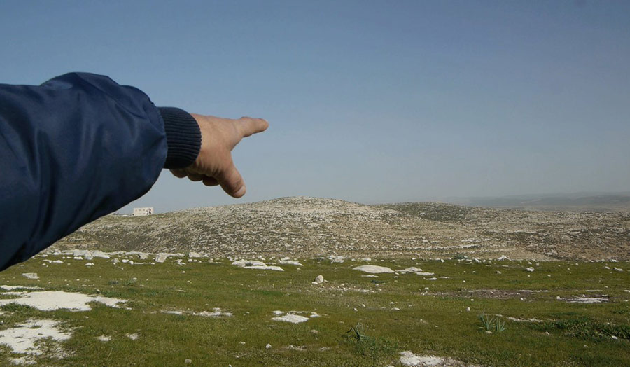 An extended arm and finger pointing to the horizon in an rural landscape