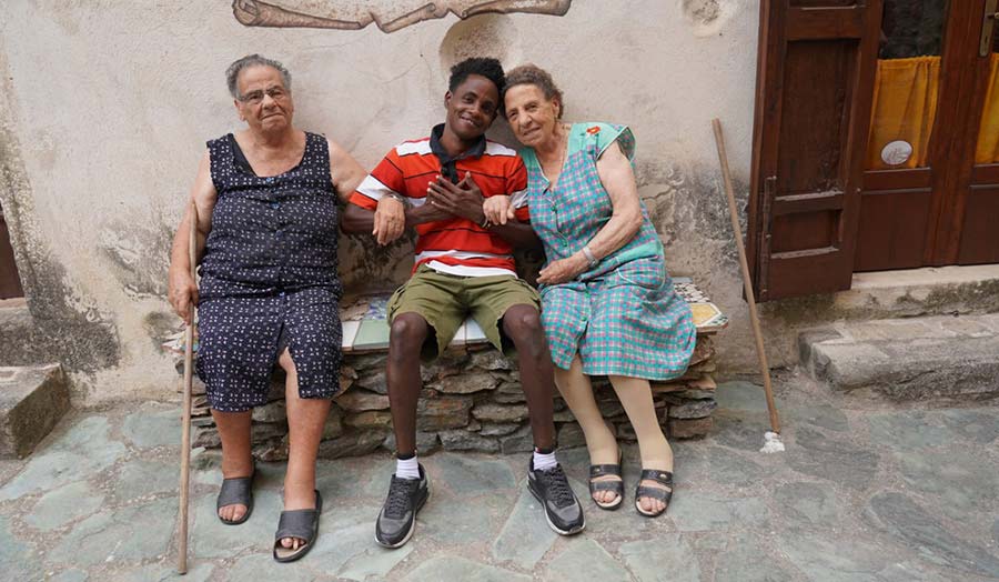 A refugee young man sitting on a bench and being embraced by two elderly women