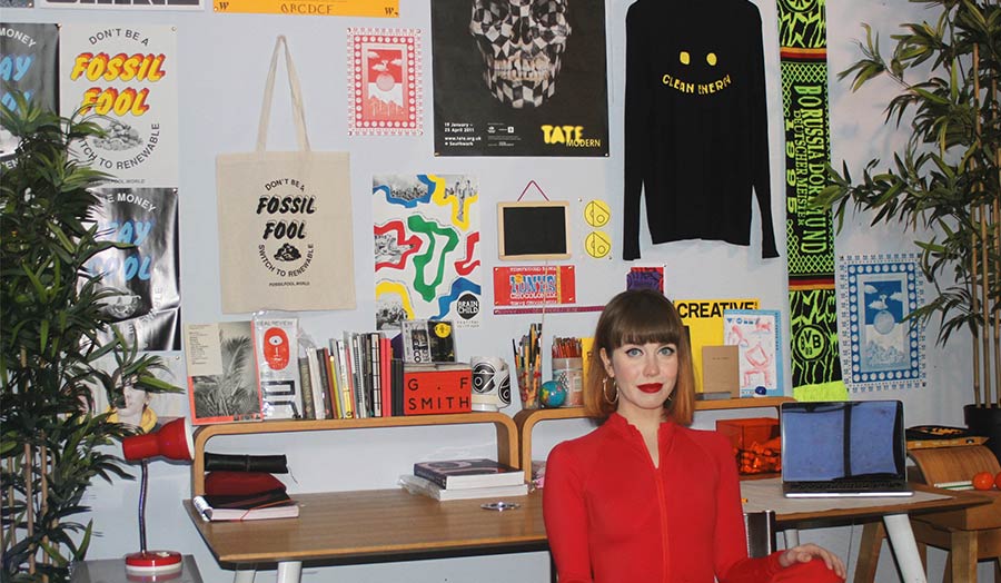 Portrait of the artist seated next to a display of her graphic design work