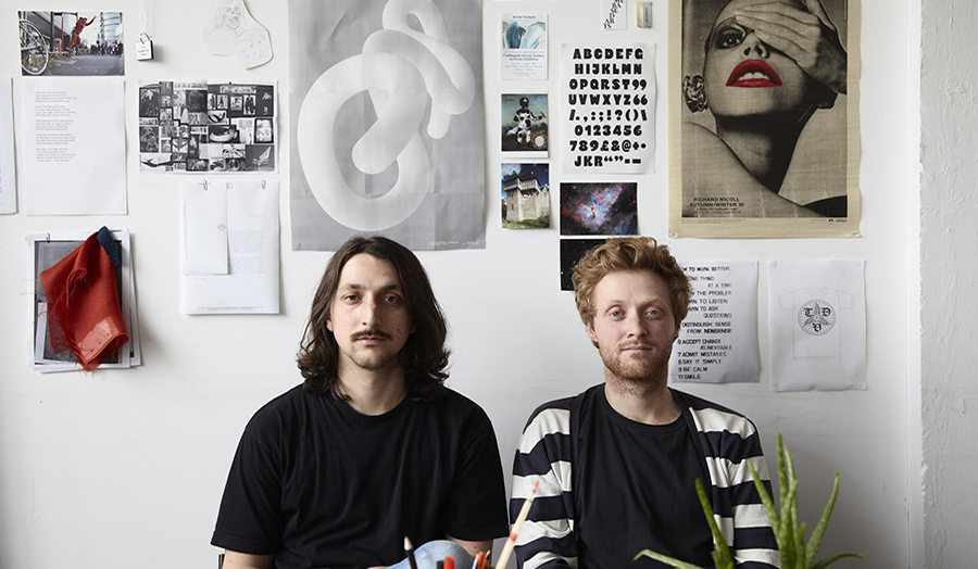 Two designers in studio with work on wall