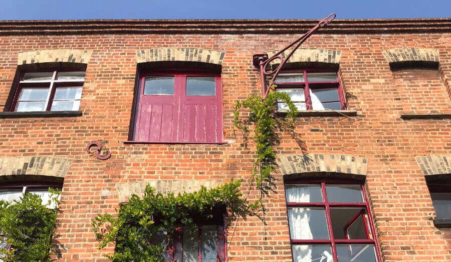 Low view of industrial brick facade with red frames and door with winch hook and climbing plant