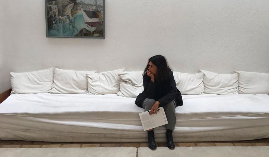 Mercedes Vicente sitting on a white sofa, looking left, with a painting in the background
