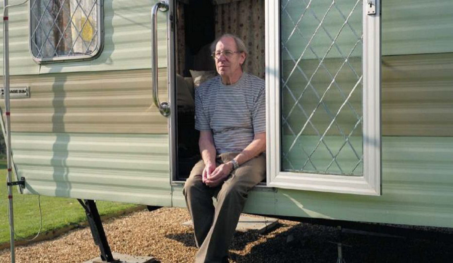  Image of man sitting by his trailer home.