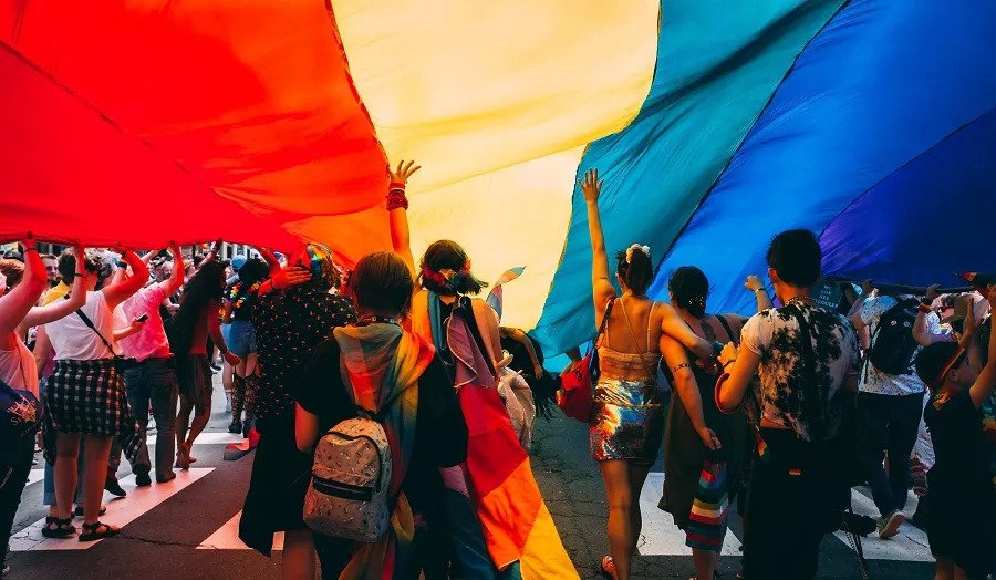 People marching together under a rainbow coloured tapestry