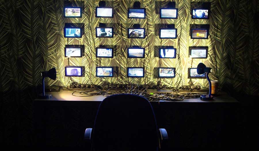 a bank of surveillance camera images on a wall in a dark room with an empty chair in front of them