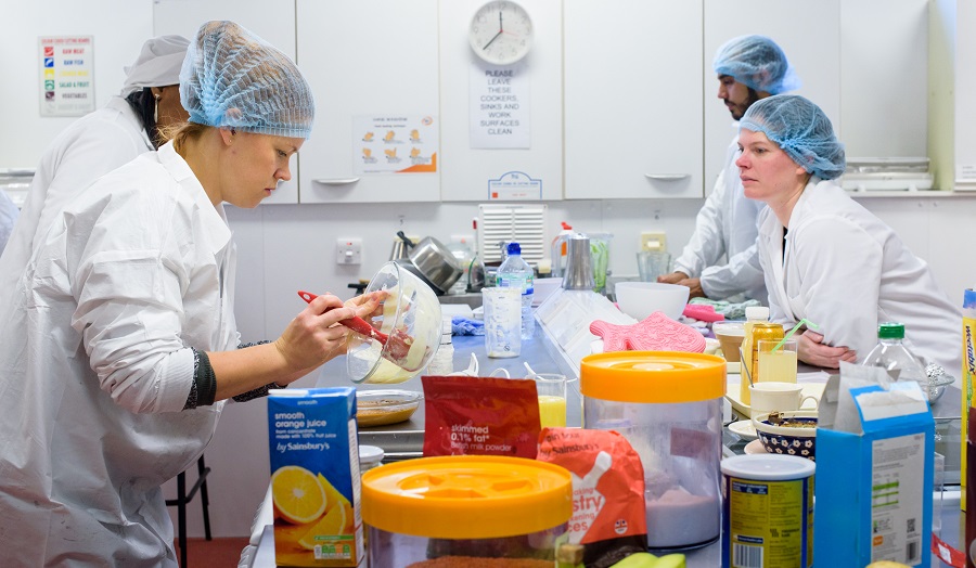 four nutrition students working in a food lab, wearing lab coats and hairnets