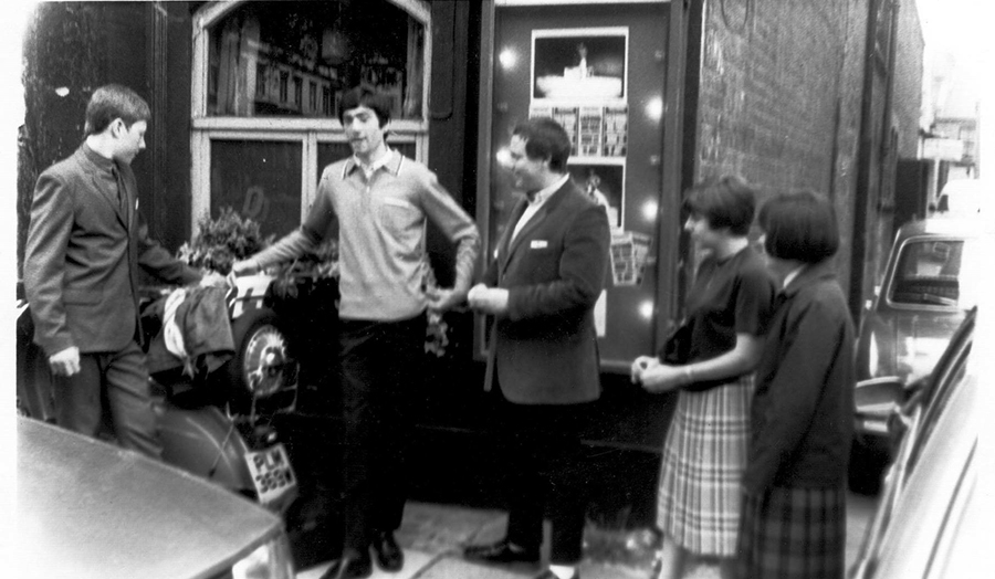Black and white image of people talking outside a shop