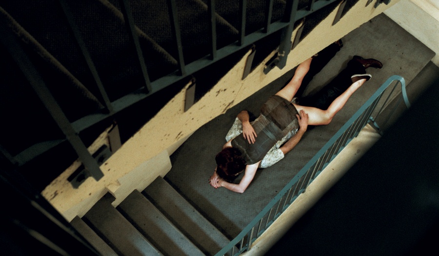 two people lying on top of each other in an empty concrete stairwell with green railings