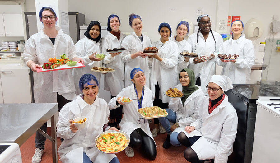 A group of students in their lab coats and hairnets happily hold finished food projects