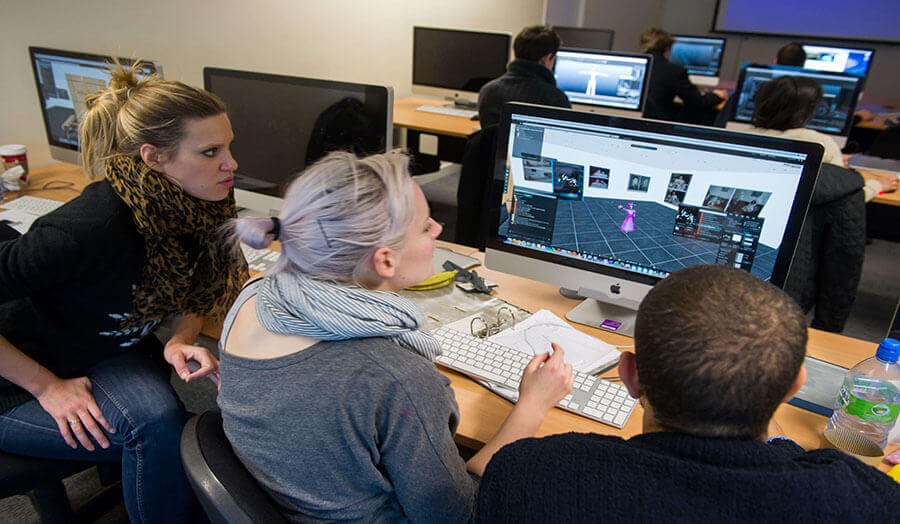 three students in front of a Mac screen working on a digital media project