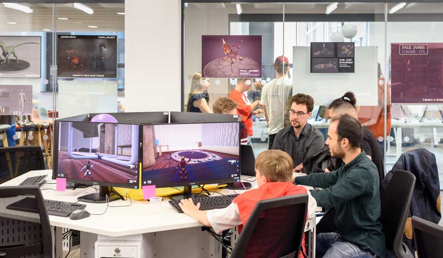 Four students sitting at a table looking at screens with computer games at Computing Summer Show