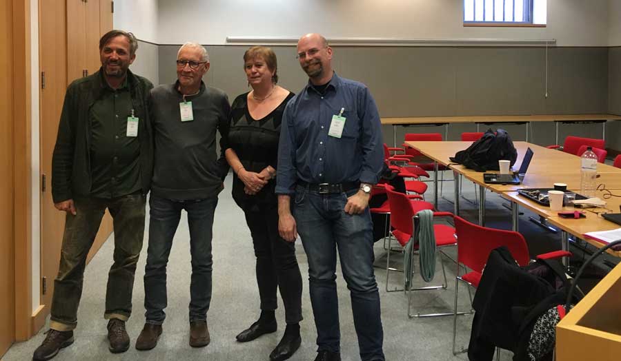 4 people from the Transnational Radio Encounters project team standing in a conference room with red chairs at the British Library