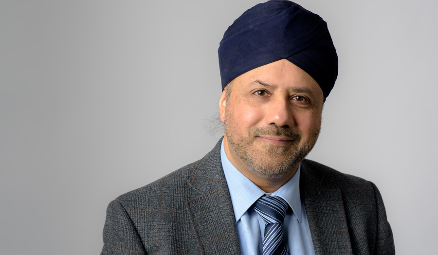 Male lecturer, Bal Virdee, gazes at the camera dressed in a suit.