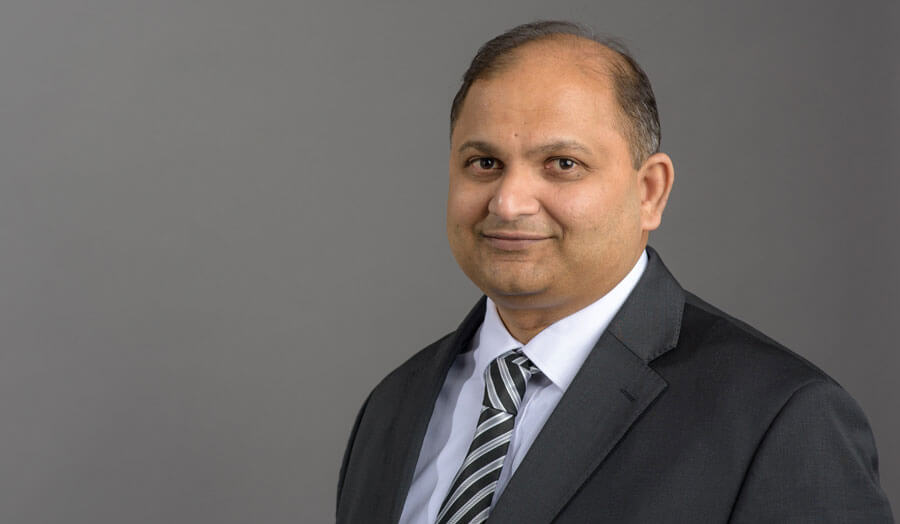 Male lecturer Pancham Shukla wears a suit as he smiles to camera.