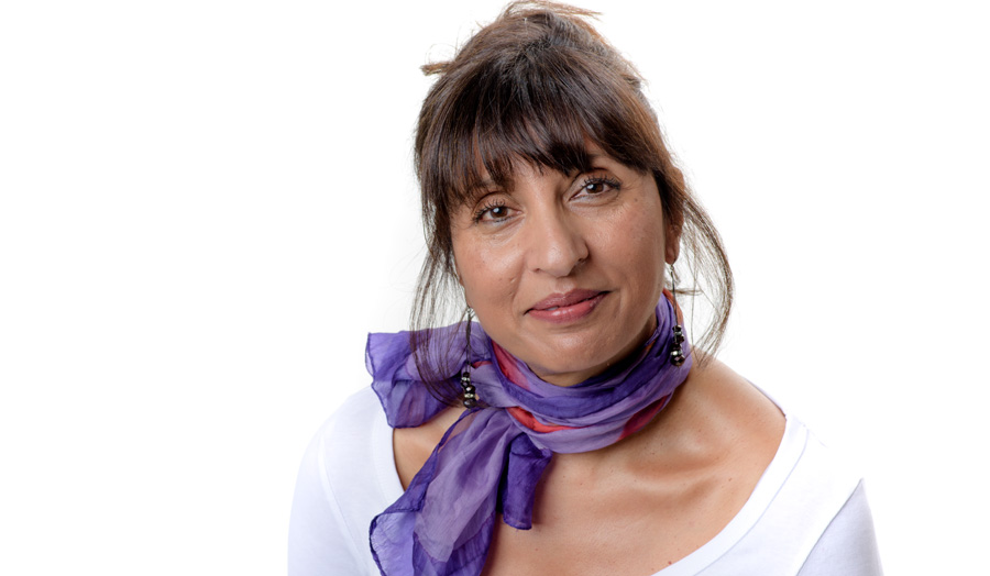 Preeti Patel wears a distinctive purple scarf as she looks to the camera with a smile.