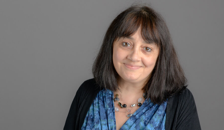 Sarah Atchia, a female lecturer with long hair, smiles gently to the camera.