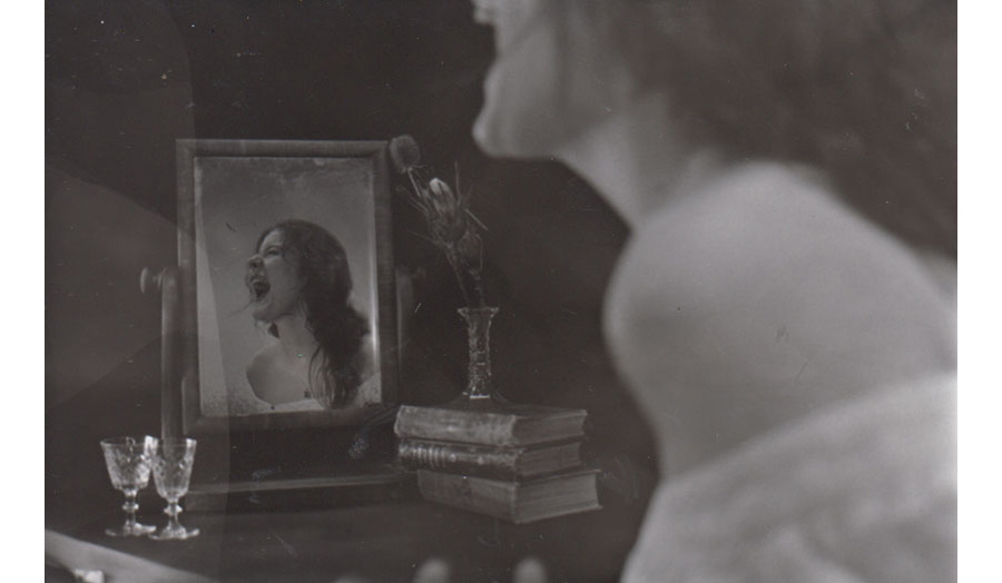 Black and white image of a student screaming in front of a mirror on a dressing table