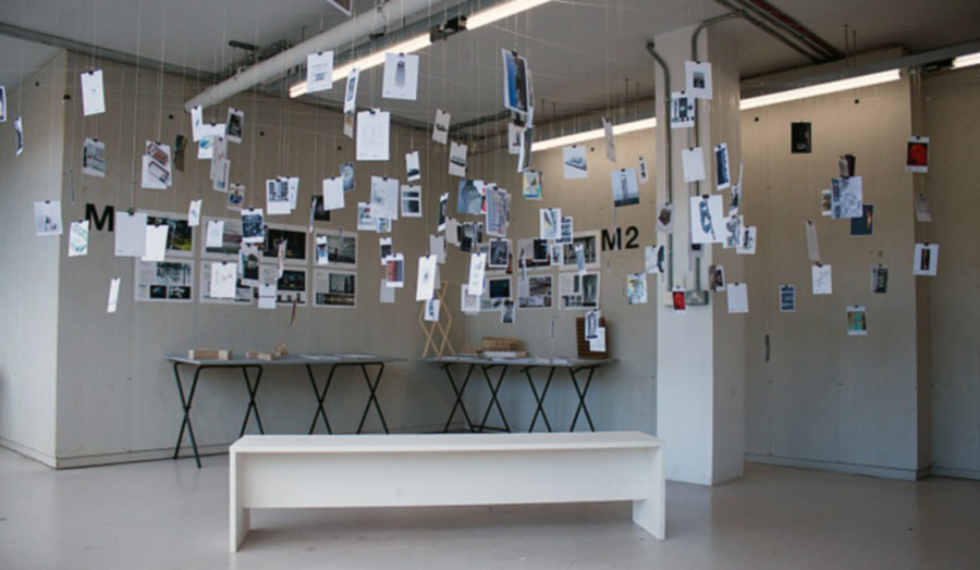 Student exhibition where papers with text and images hang from the ceiling