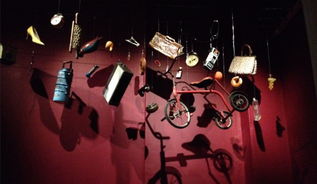 A photograph of hanging artwork containing everyday objects such as a bicycle and a cheese grater
