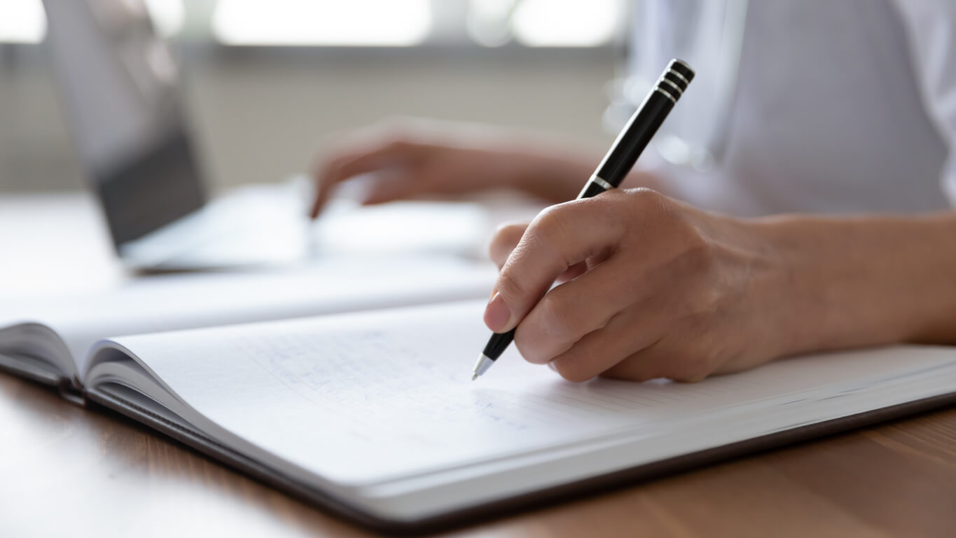 left hand writing in a notebook and right hand on the laptop keyboard