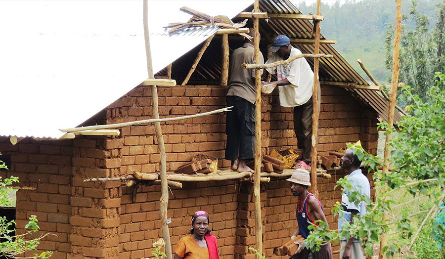 Cooperative members climb the timber pole scaffold to lay the last row of CEBs