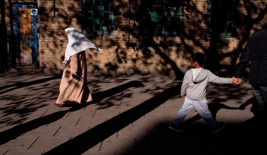 Image of two people, one child and one covered person walking by