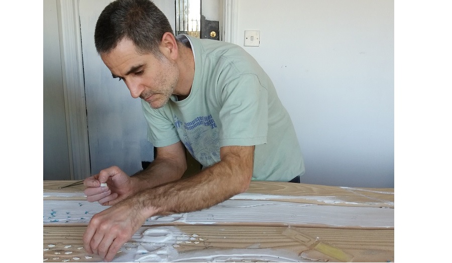 A man in a t shirt leans over a work bench working with clay