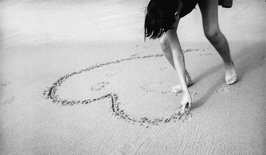 A girl draws a heart shape in the sand