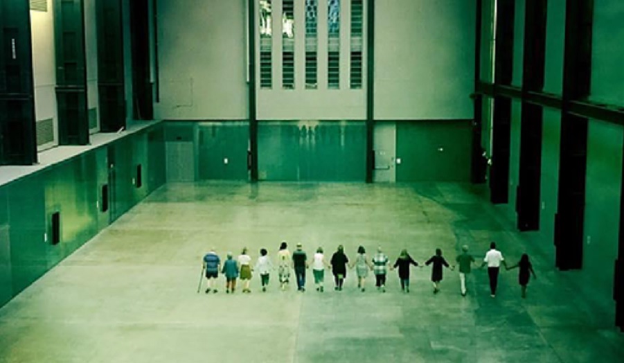 a line of people walk in tate turbine hall