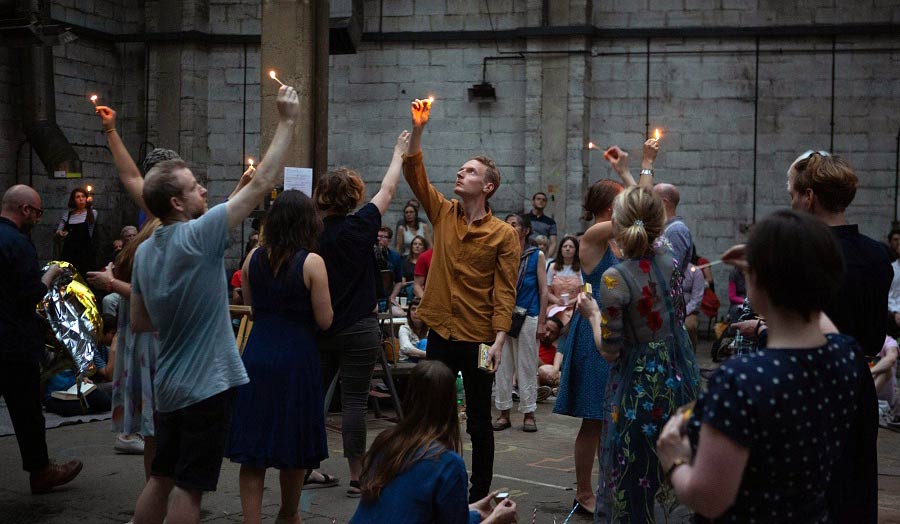 A gathering of people with their arms raised up holding a candle