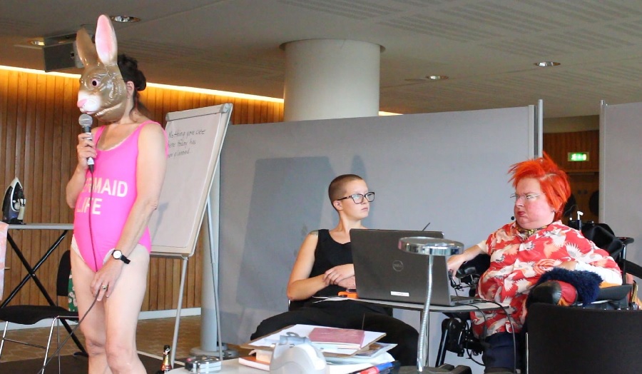 live art featuring a woman in swimsuit and donkey mask, a seated woman and a woman in a wheelchair