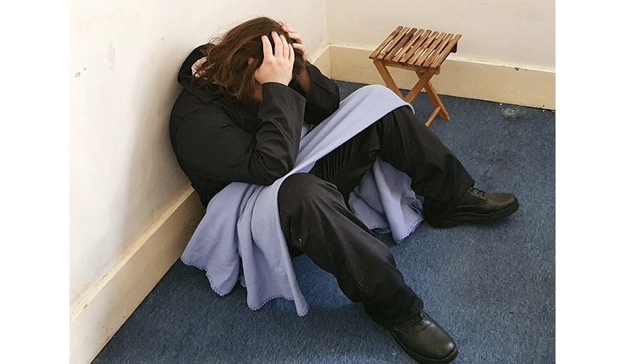 A young man sitting on the floor, head down and hands on head