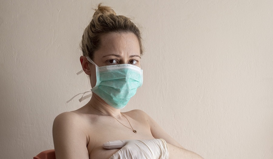 photograph of woman in facemask, gloved hand on pregnant belly