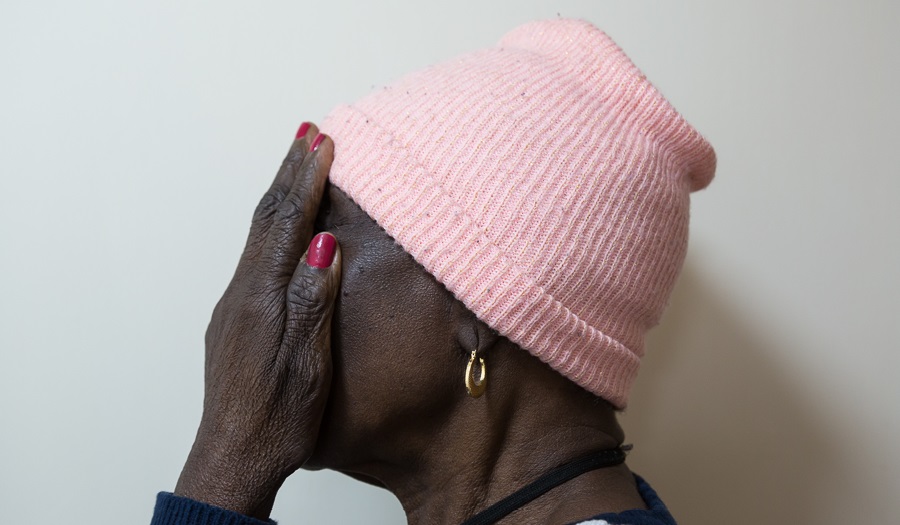 woman in pink hat and gold earrings seen from side holds hands over her face