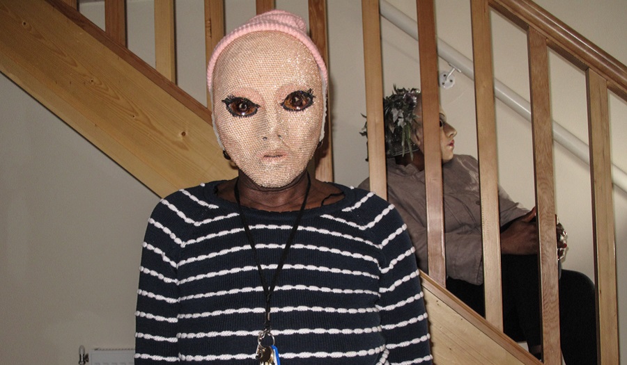 woman in pale mask and striped jumper looks towards camera