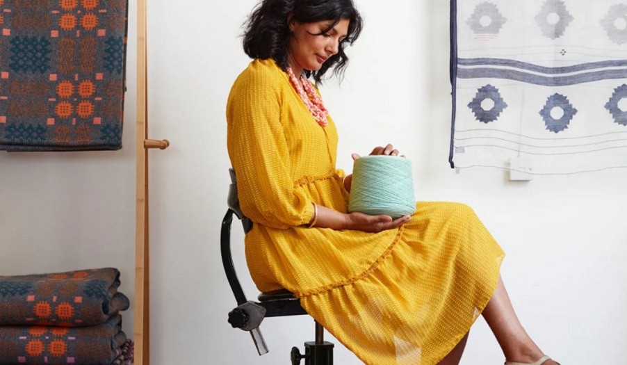 woman in yellow dress sits holding roll of yarn