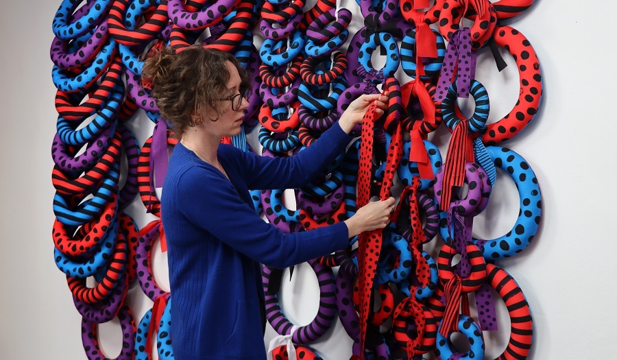 Woman stands with blue and red looped textile structure