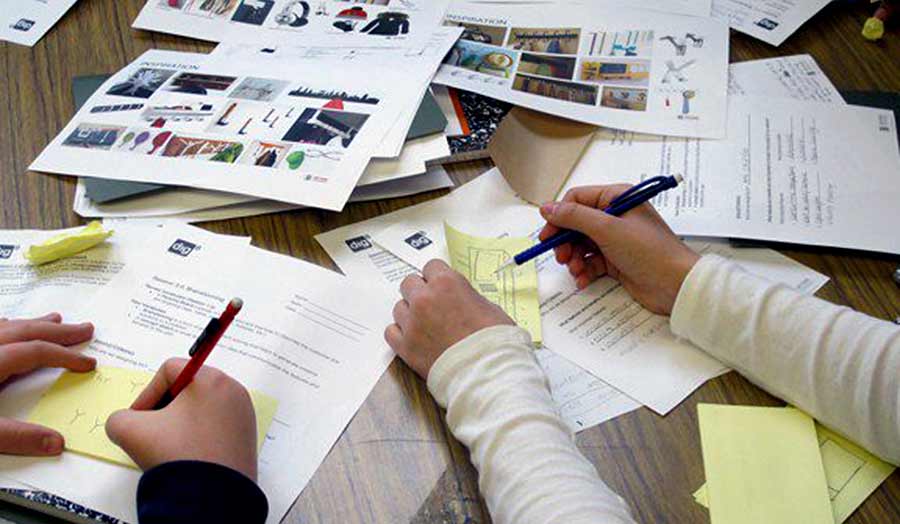 A view of hands of 2 people with pens and working on a table