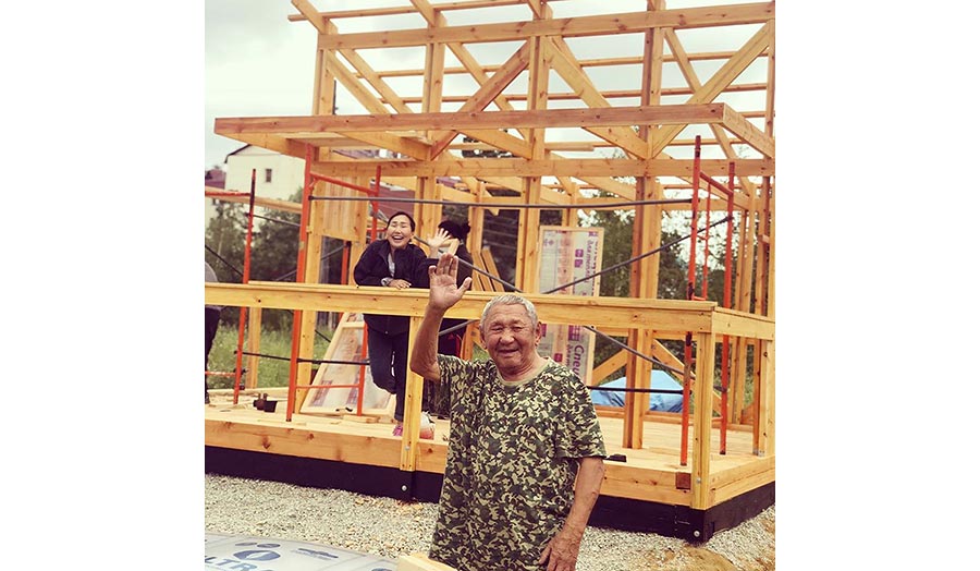 An old man and a woman saluting from a wooden architectural structure