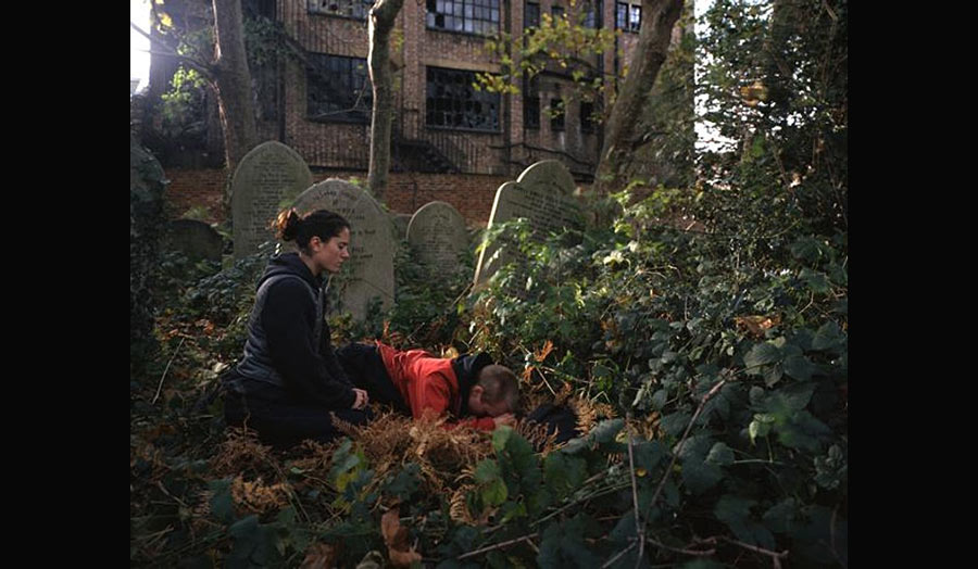 A man and a woman kneeling in the cemetery in front of a grave