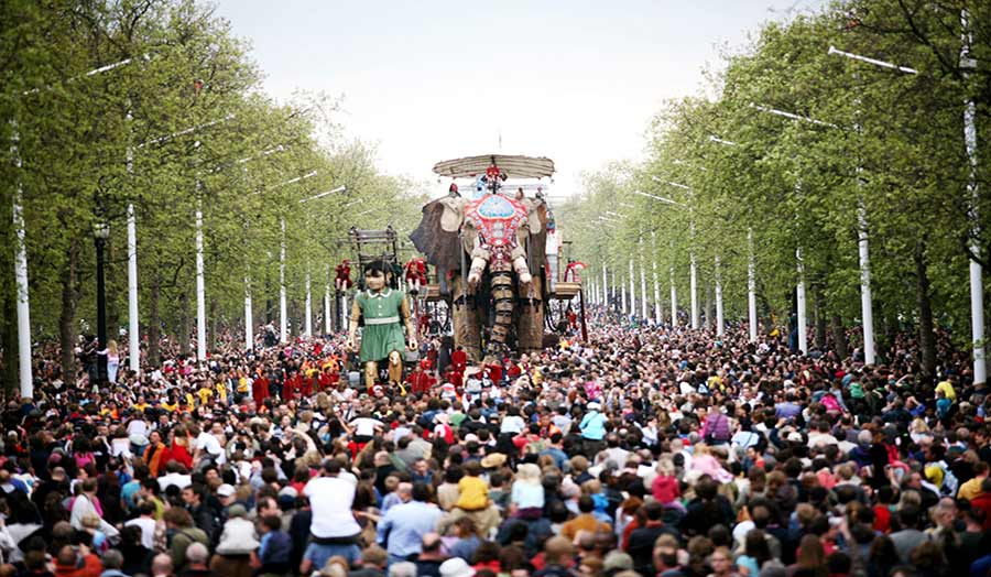 A large sculpture of an elephant is carried among a crowd of people.