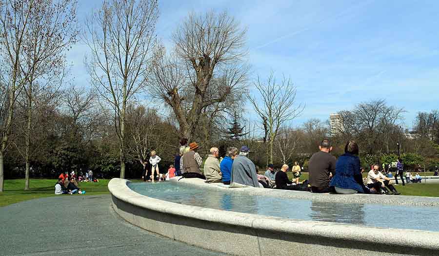 People sit on the stone edge of a water feature in Hyde Park